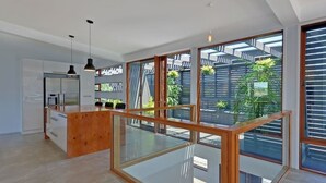 A modern kitchen with a wooden island, large windows, and a view of greenery outside. - Amazing Unique Five-Star Waterfront Retreat (Old Beach)