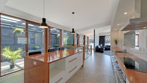 A modern kitchen with a central island, large windows, and a dining area with a sofa. - Amazing Unique Five-Star Waterfront Retreat (Old Beach)
