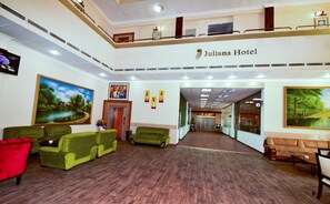 Eine Hotelhalle mit grünen Sofas, einem roten Sessel und Bildern an den Wänden.