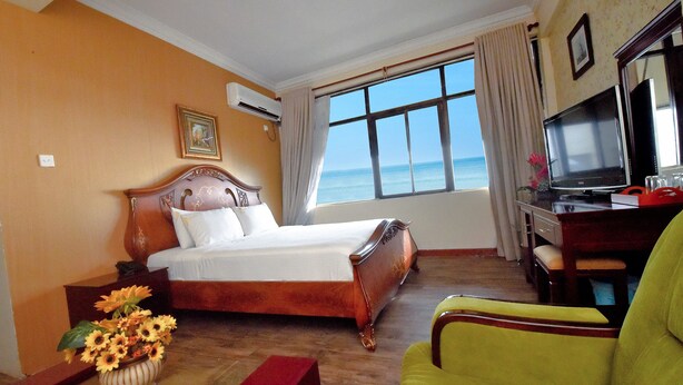Une chambre d’hôtel avec un lit, un bureau avec une télévision, une chaise et une vue sur l’océan.