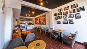 Un café chaleureux avec des tables et des chaises en bois, un comptoir où l’on sert du café et un mur décoré de tableaux encadrés.