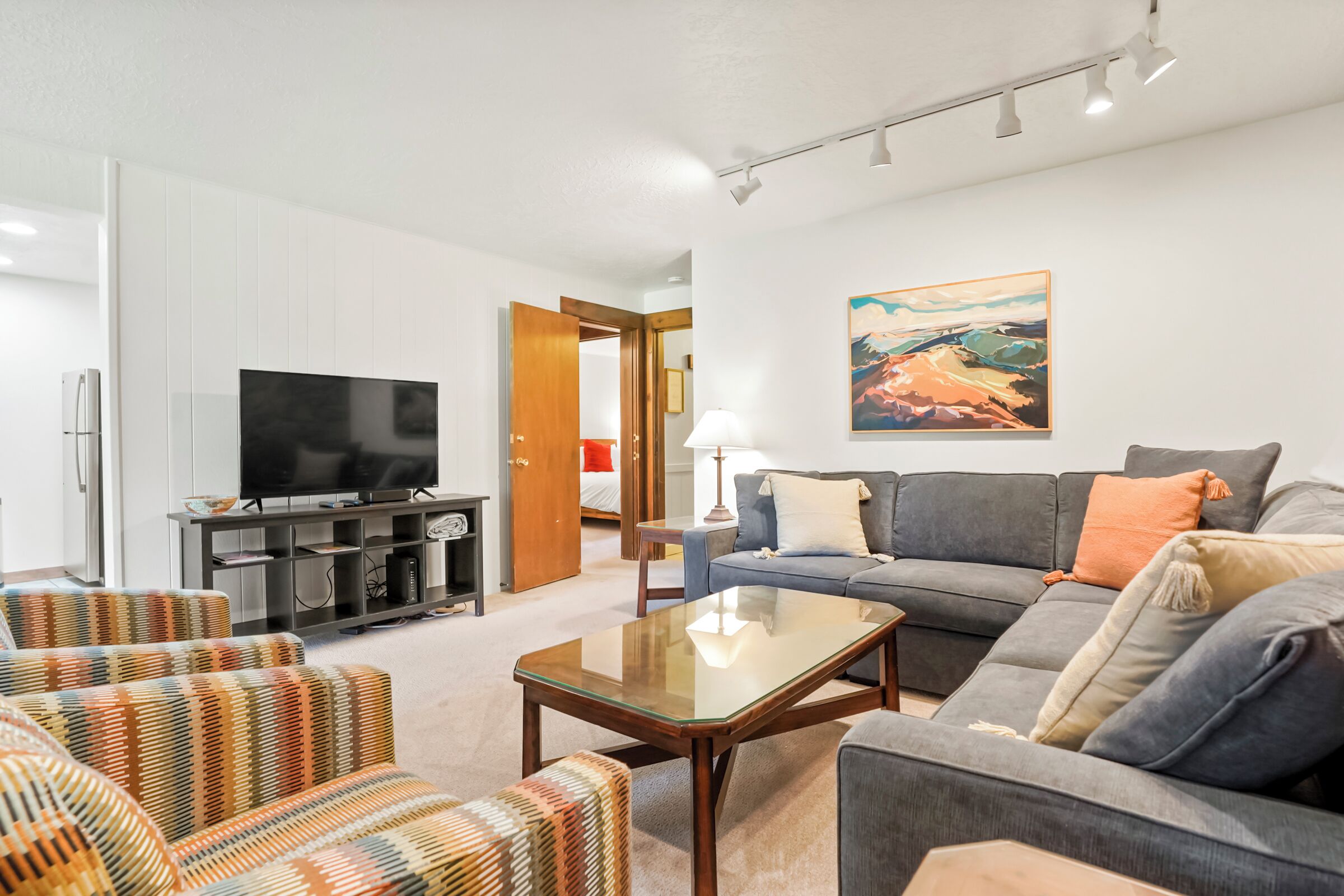 A modern living room with a flat-screen TV, sofa, and patterned chairs.