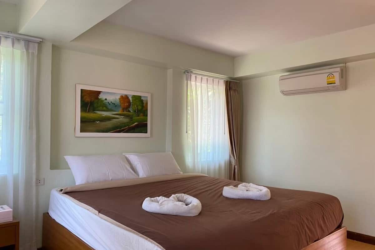 Ein Hotelzimmer mit einem großen Bett, weißen Kissen, einem Landschaftsbild und einem Fenster mit Vorhängen.