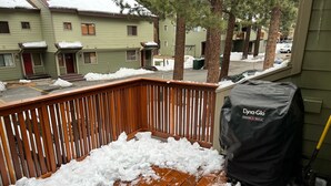 Une terrasse en bois recouverte de neige, une housse de protection pour barbecue et, au fond, un immeuble d’habitation.