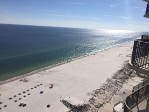 Une vue sur la plage depuis un balcon, avec un ciel dégagé, une plage de sable et quelques parasols et chaises longues.