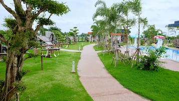 A pathway leading to a pool area surrounded by lush greenery and a large tree.