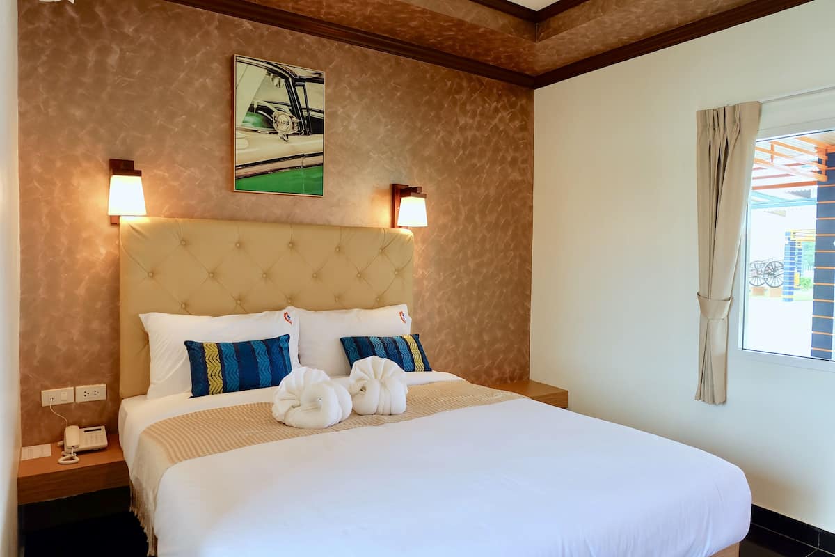 A hotel room with a large bed, two wall-mounted lamps, a framed picture above the bed, and a window with curtains.