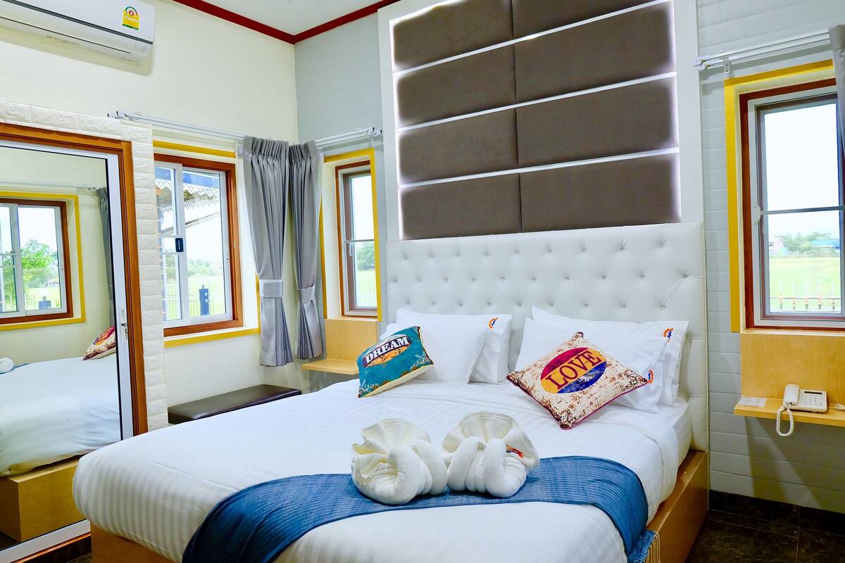 A hotel room with a large bed, a bedside table, a mirror, and a window with curtains.
