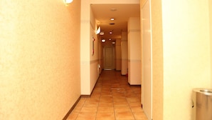 Un couloir d’hôtel avec un sol carrelé, des appliques murales et une poubelle.
