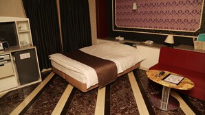 Une chambre d’hôtel avec un lit, un bureau avec un téléphone, une petite table avec une lampe et un canapé rouge.