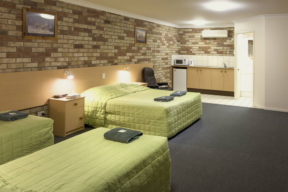 A hotel room with two beds, a desk, a chair, a microwave, and a small kitchenette.