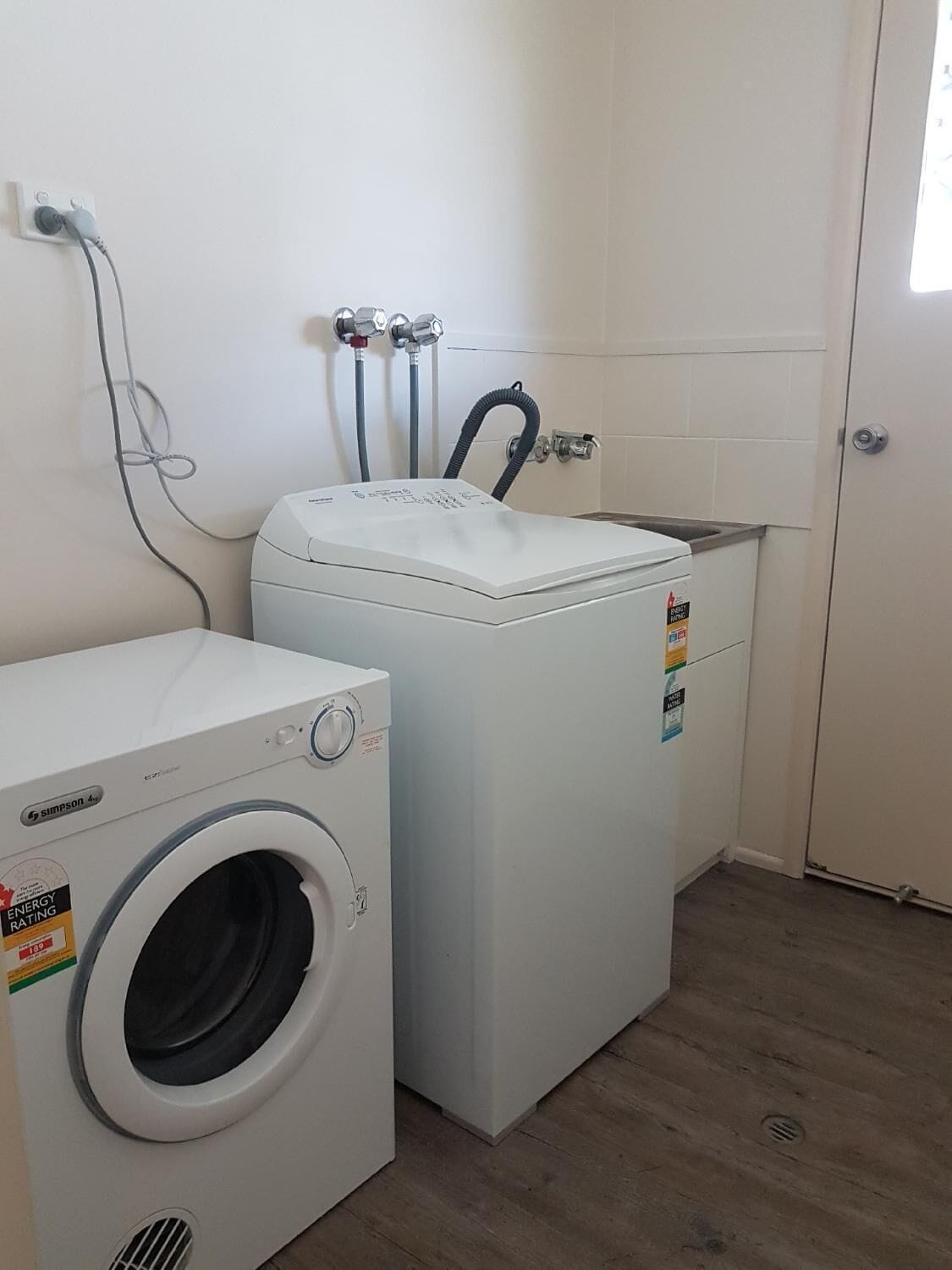Uma lavanderia com máquina de lavar e secar de abertura frontal, aquecedor de água e pia.