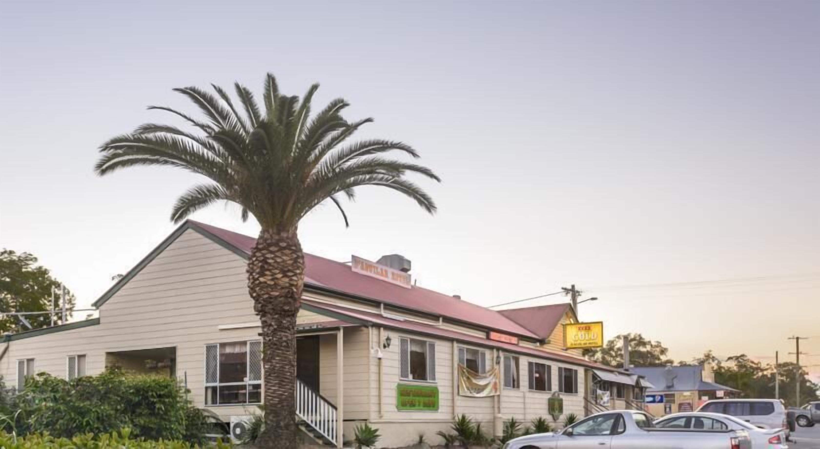 A two-story building with a red roof and a large palm tree in front. There are cars parked in front and a sign that says "GOLD".