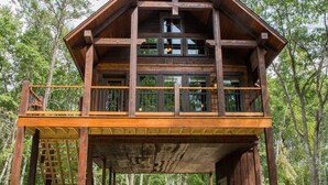 A two-story wooden cabin with a balcony, surrounded by trees. - Elevate Your Stay! (Crosslake)