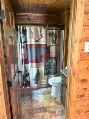A compact bathroom with a shower curtain featuring wildlife prints, a toilet, and a wooden floor. - Elevate Your Stay! (Crosslake)