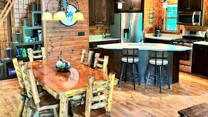 A rustic cabin interior with a wooden dining table, chairs, a kitchen area, and a staircase. - Elevate Your Stay! (Crosslake)