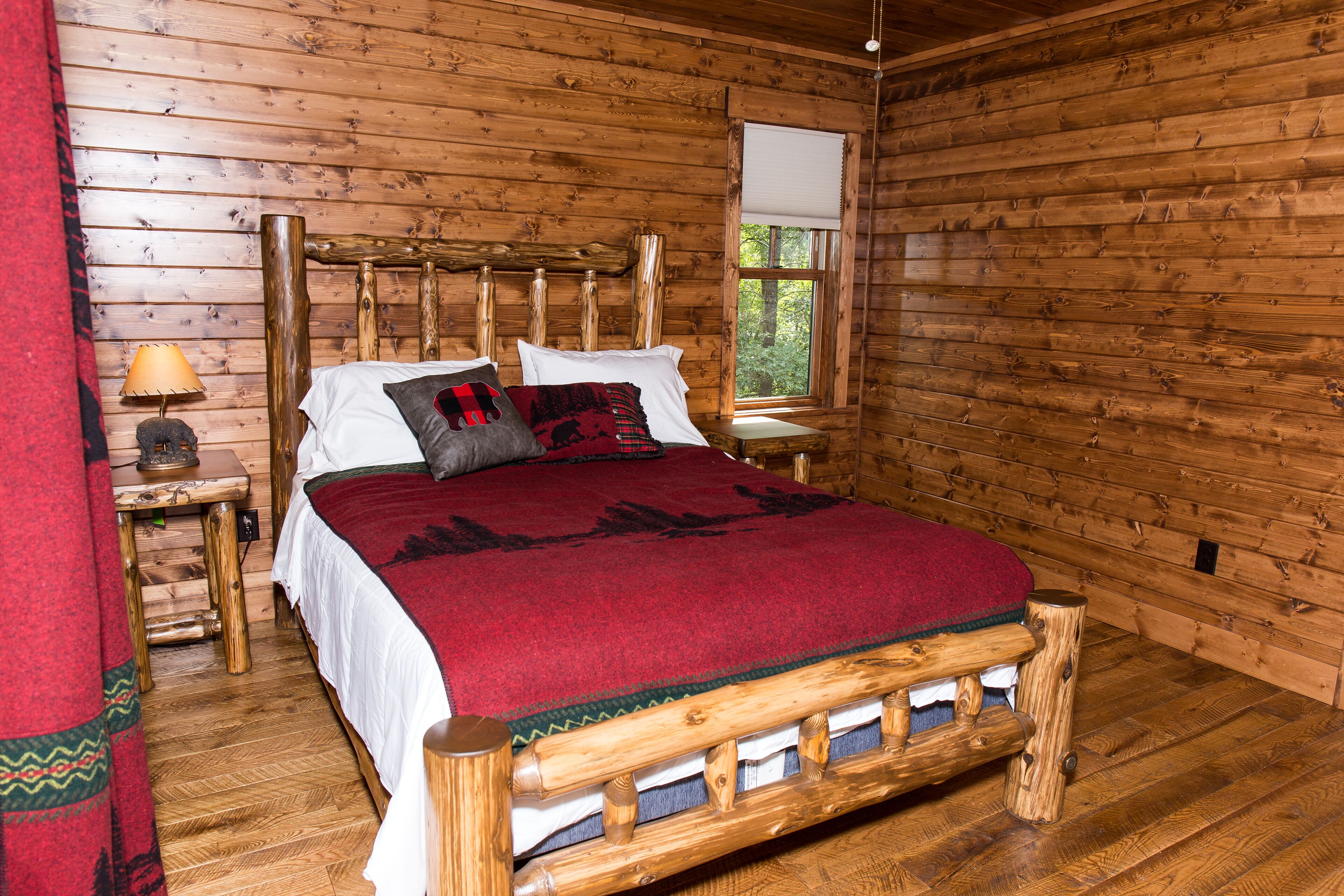 Une chambre à coucher dans une cabane en bois, avec un lit, une table de chevet, une fenêtre et une vue sur l’extérieur.