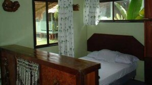 A bedroom with a bed, a wooden dresser, a ceiling fan, and a window with a view of greenery outside.