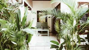 A spacious indoor area with a tiled floor, a light blue bench, and various green plants. - Kalua Boutique Bungalows (Gili Trawangan)
