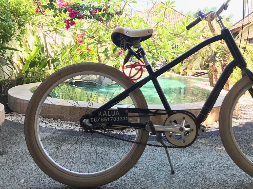 Een fiets met een zichtbaar serienummer, geparkeerd nabij een zwembad met een tropische tuin op de achtergrond.