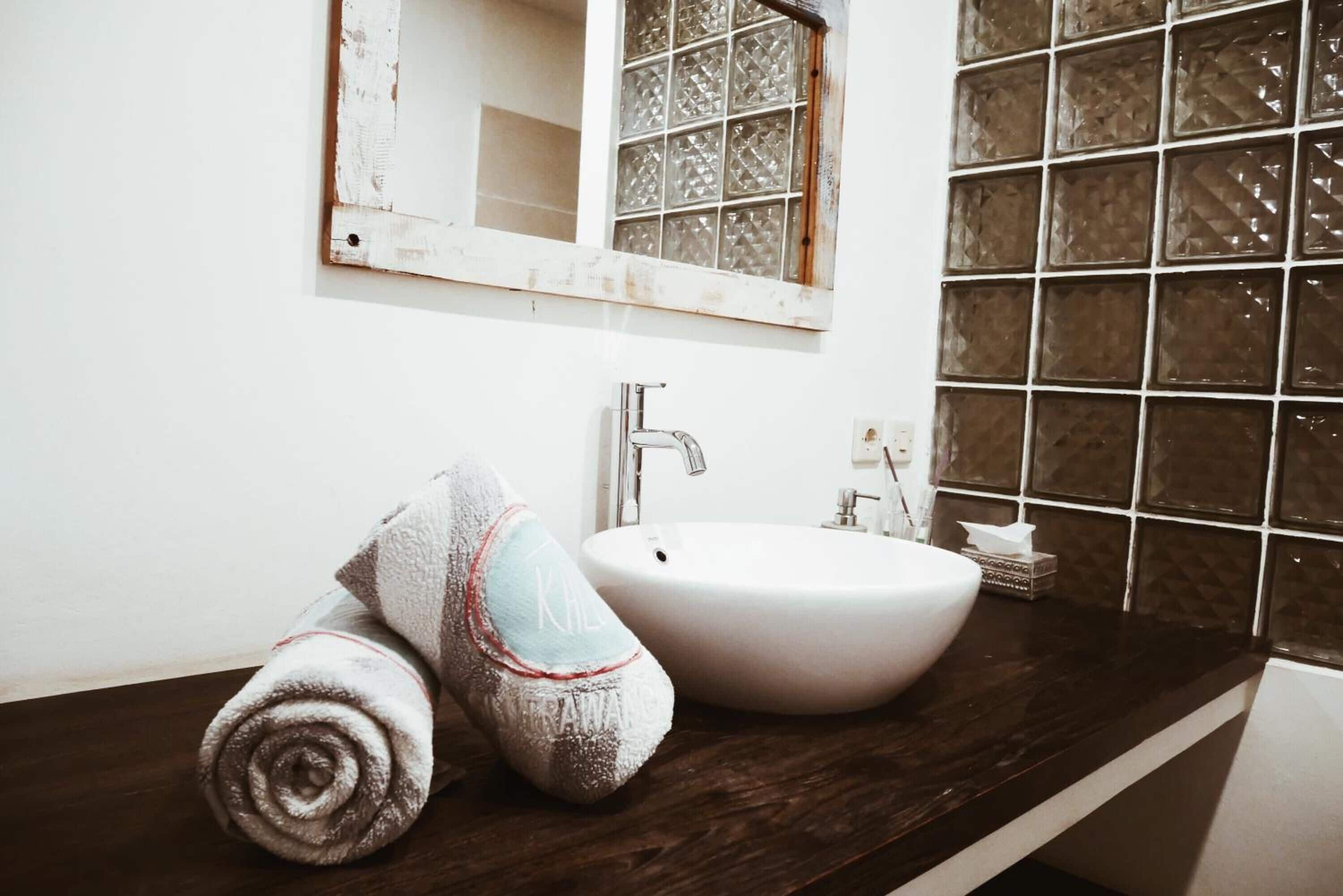 Un baño con un lavamanos blanco, un espejo y un ventanal con paneles de vidrio decorativos.