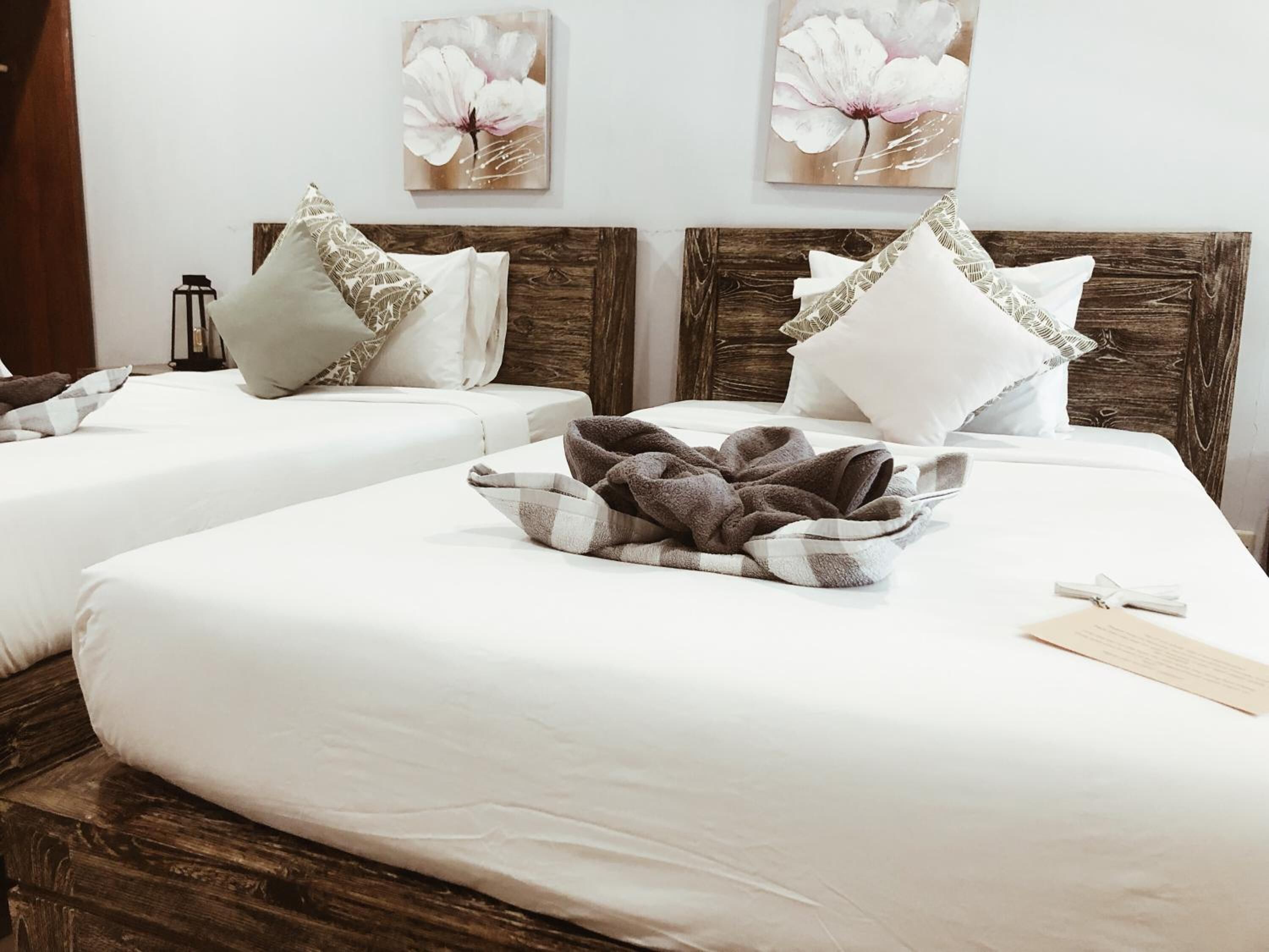 A hotel room with two beds, each with white bedding and decorative pillows. There are two wall-mounted flower paintings above the beds.