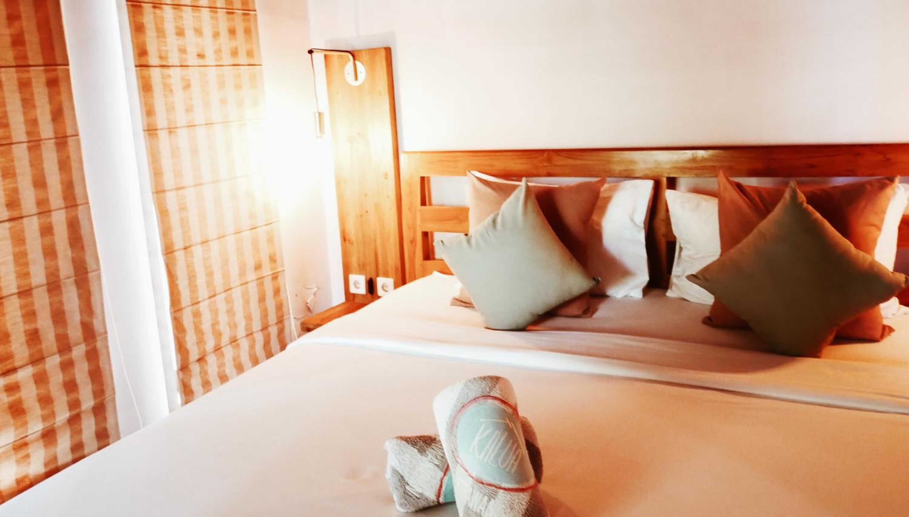 Een net opgemaakt bed met een houten hoofdbord, twee kussens en een opgerolde handdoek.