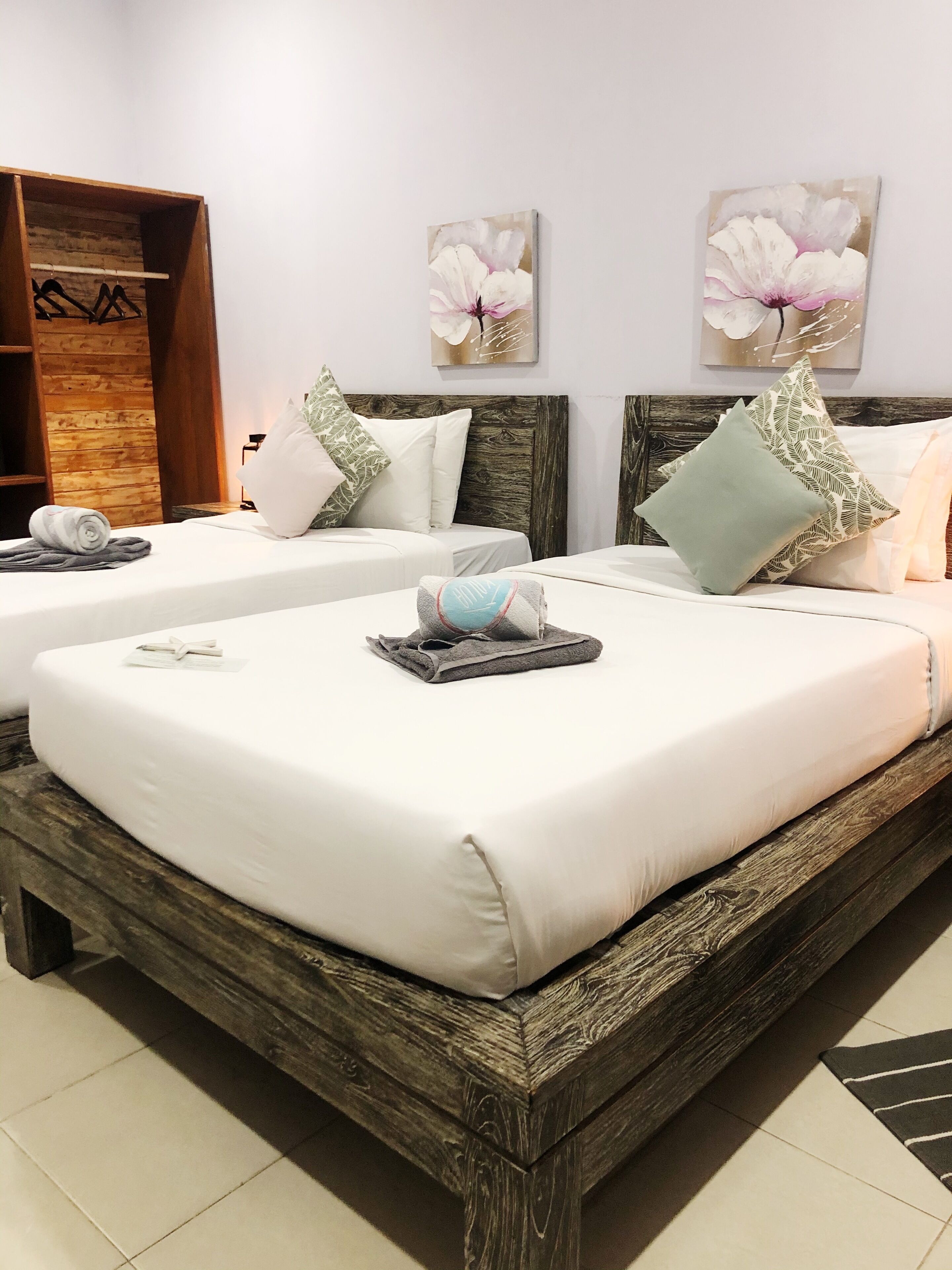 Habitación de hotel con una cama grande, dos camas más pequeñas, cabeceras de madera, ropa de cama blanca y un armario de madera.