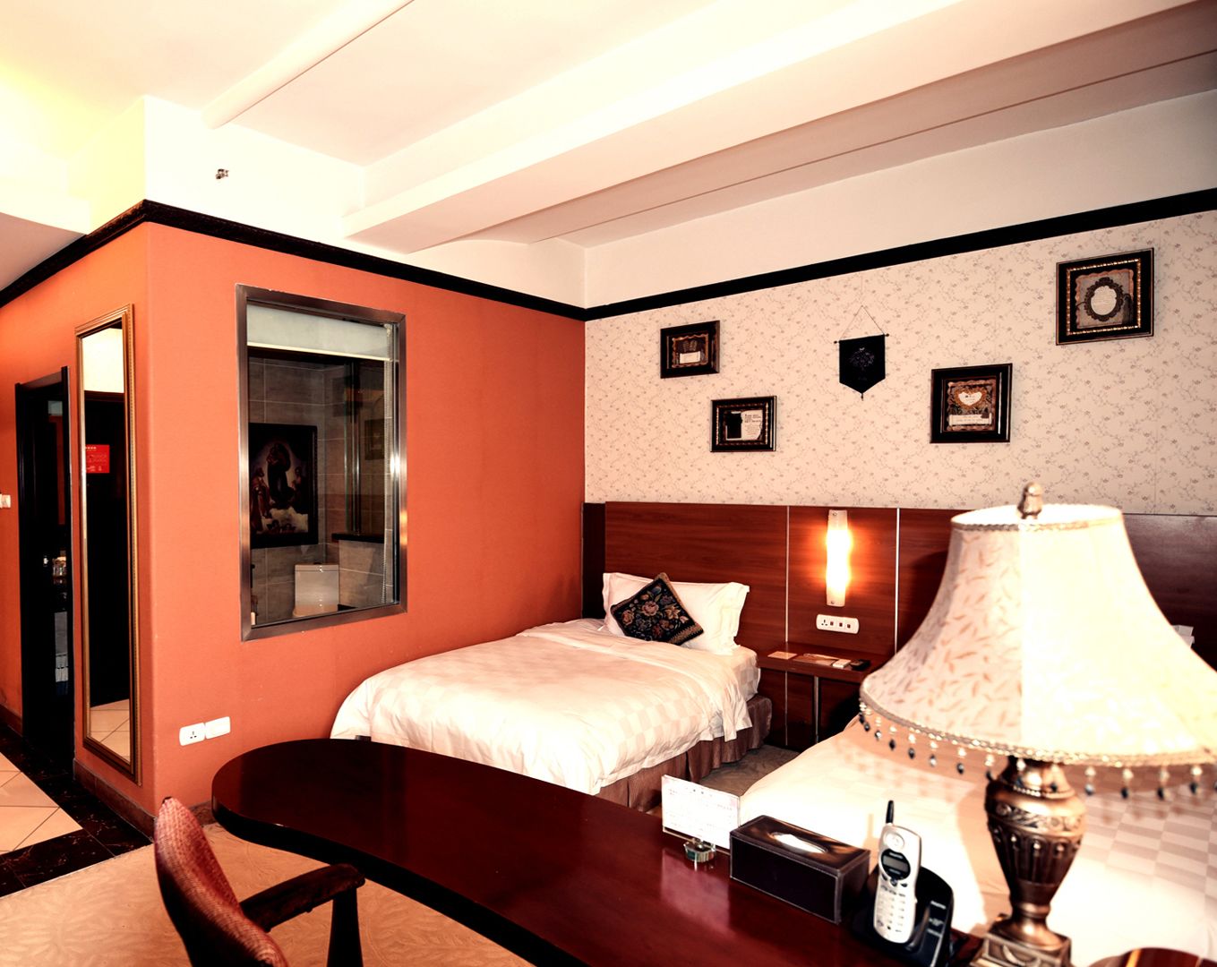 Quarto de hotel com duas camas, uma escrivaninha, um telefone e uma luminária.