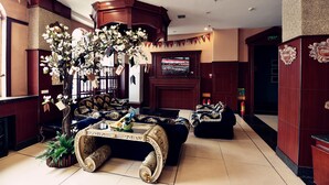 A lobby with a grand staircase, a large floral arrangement, and a television screen displaying a sports event. - Harbin Bremen Jewish Culture Theme Hotel (Harbin)