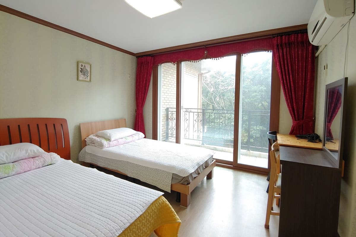 A hotel room with two beds, a desk, and a balcony with red curtains.