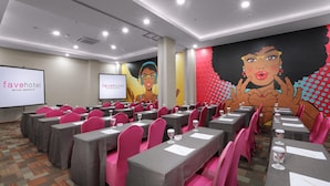 Un salón de conferencias con mesas dispuestas para una reunión, equipado con micrófonos y proyectores, y un mural grande en la pared.