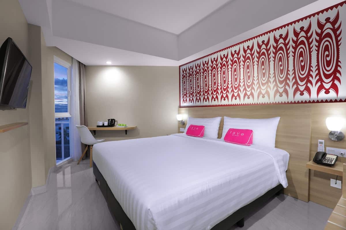 Habitación de hotel con una cama grande, un escritorio con silla, televisor, ventana con cortinas y un panel decorativo en la pared.