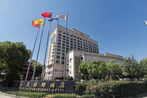 A hotel with a prominent entrance, flagpoles, and a clear sky. - Meigaomei International Hotel (Kunshan Lujia) (Kunshan)