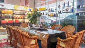 Un interior moderno con sillones de mimbre alrededor de una mesa de mármol, estantes de cristal con objetos decorativos, y un coche visible a través del muro de cristal.