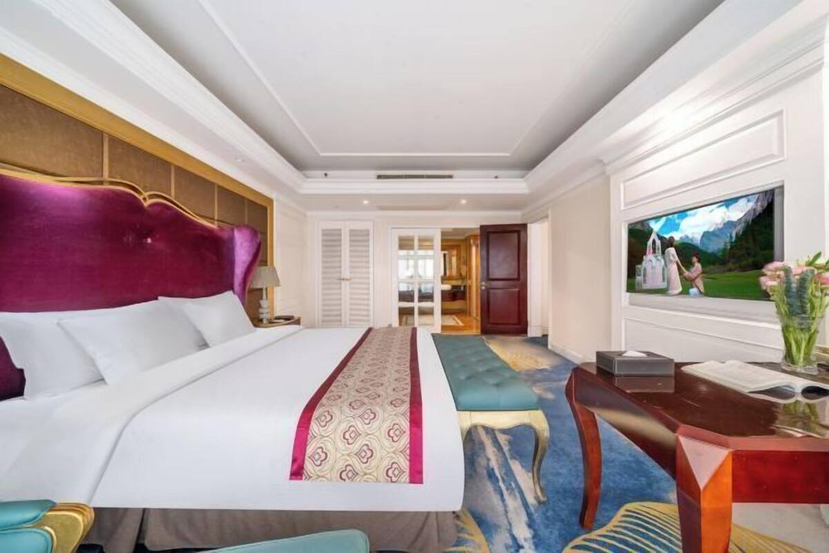 A hotel room with a large bed, a desk with a vase, and a television on the wall.