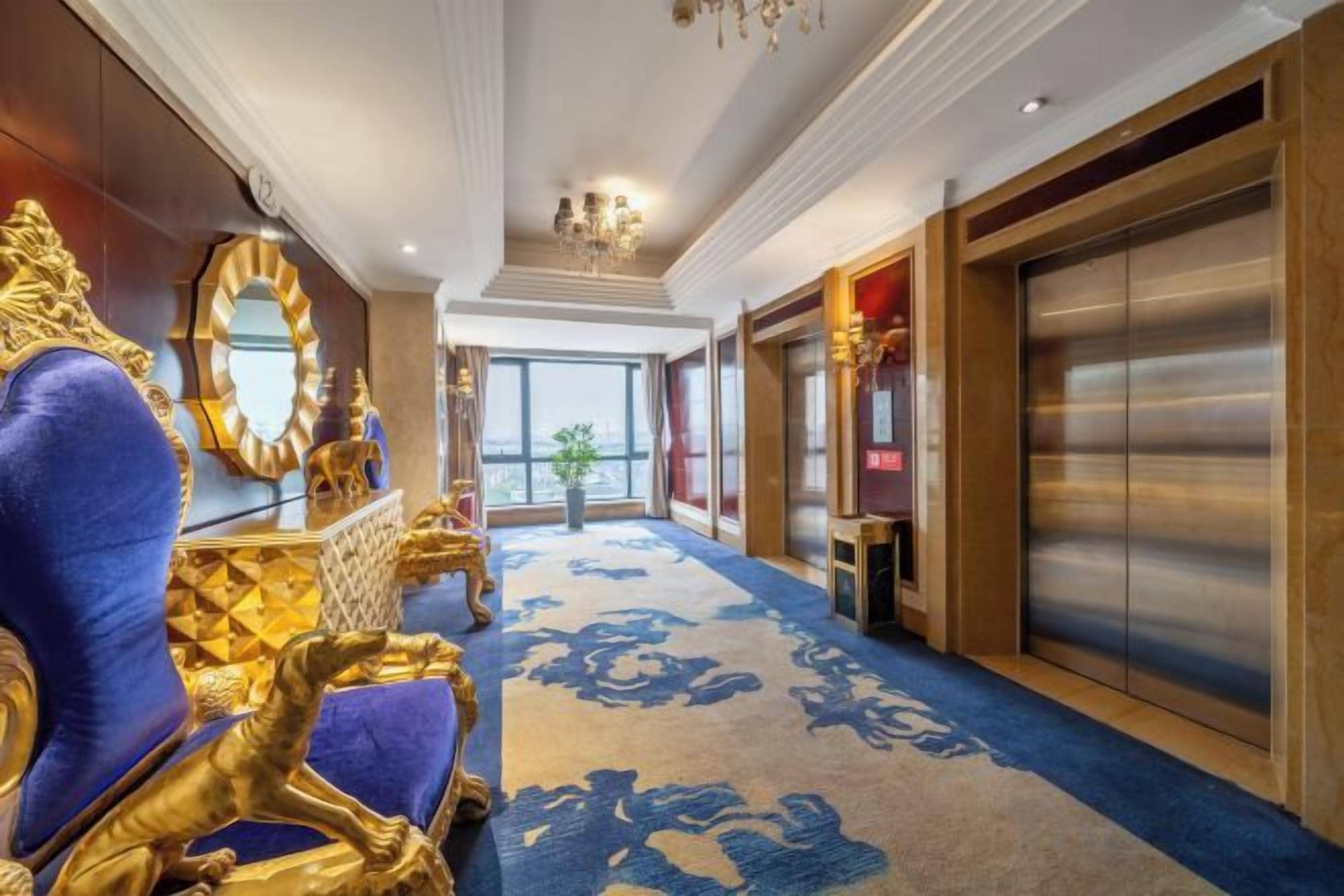 A luxurious hotel lobby with ornate gold furniture, a large mirror, and a modern elevator.