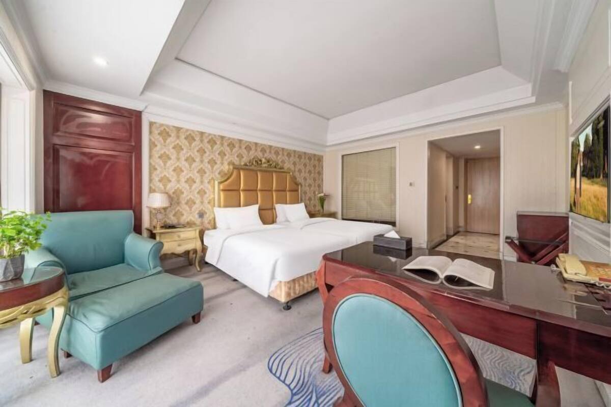 A hotel room with a bed, a desk, a chair, a sofa, and a small table with a plant.