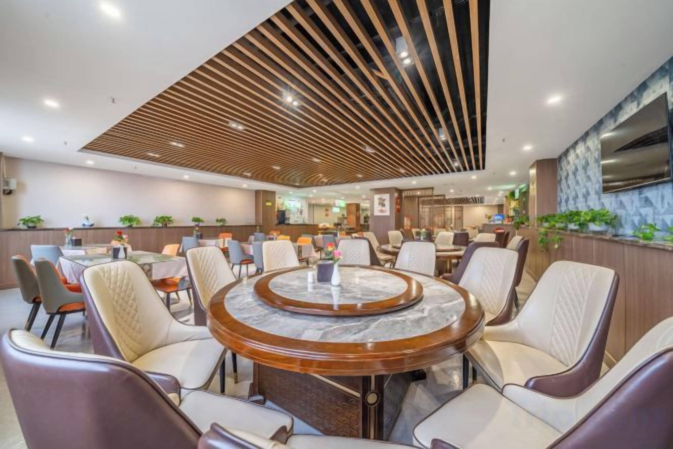 Un comedor moderno con una mesa redonda de mármol rodeada de sillas de cuero, techo de madera con listones y vista a la cocina al fondo.