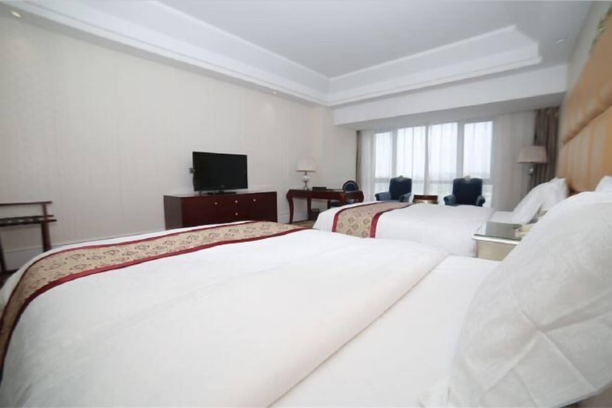 A hotel room with two beds, a TV, a desk, and a window with curtains.