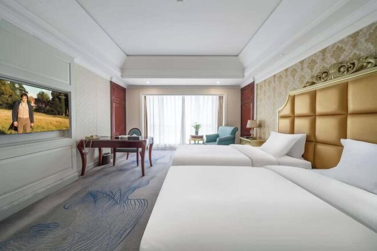 A hotel room with a large bed, a desk, a chair, and a television.
