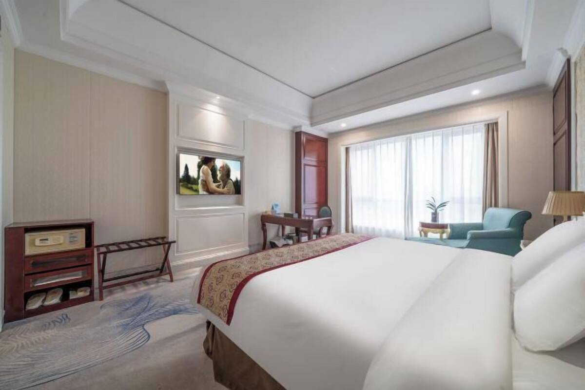 A hotel room with a large bed, a desk, a chair, a TV, and a window with curtains.
