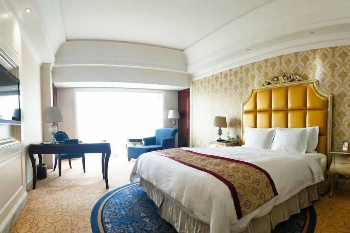A hotel room with a large bed, a desk, two chairs, and a view of the outdoors.