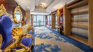 Un pasillo lujoso con alfombra azul, muebles dorados y un espejo grande.