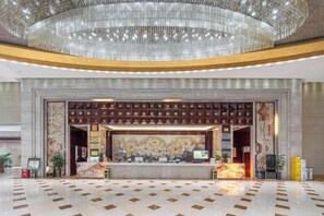 A hotel lobby with a reception desk, a large chandelier, and a patterned wall. - Meigaomei International Hotel (Kunshan Lujia) (Kunshan)