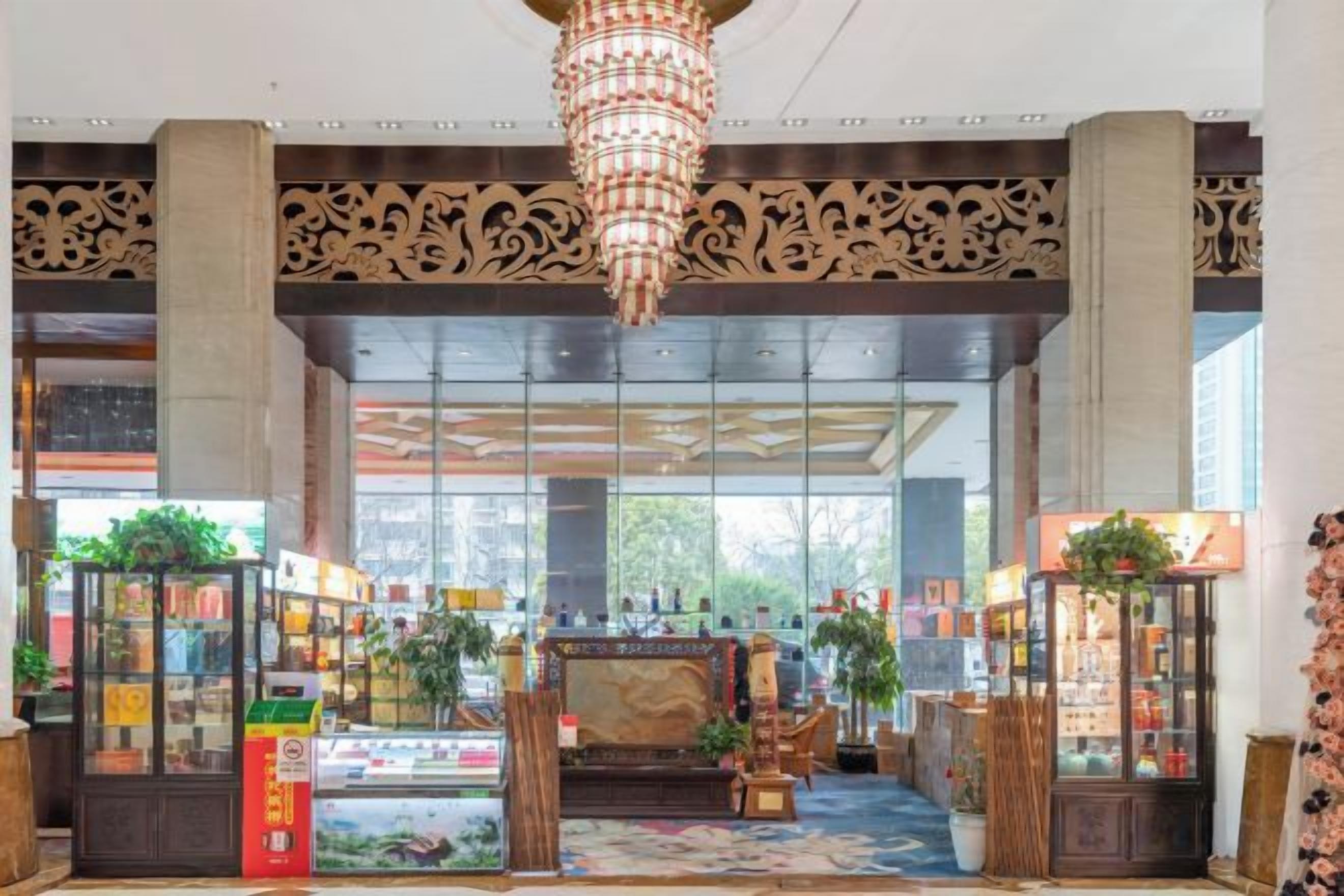 A lobby with a chandelier, large windows, and a central area with plants and a display case.