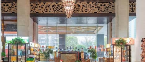 A lobby with a chandelier, large windows, and a central area with plants and a display case.