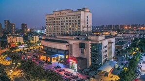 Un hotel de varios pisos con estacionamiento y edificios comerciales contiguos.