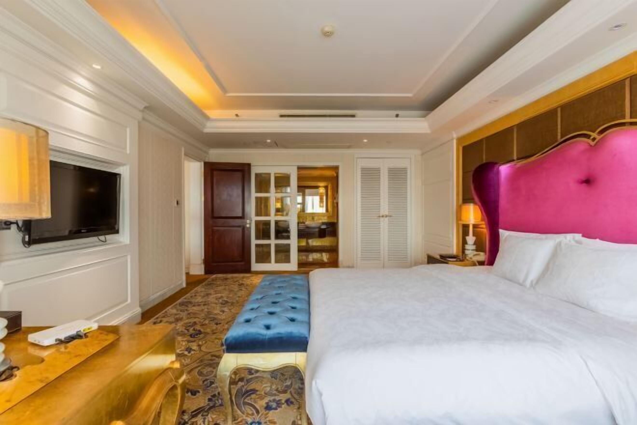 Una habitación de hotel con una cama grande, televisión, escritorio de madera y alfombra estampada.