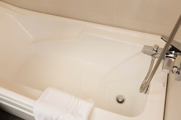 Une baignoire équipée d’un pommeau de douche à main et d’une serviette placée à côté.